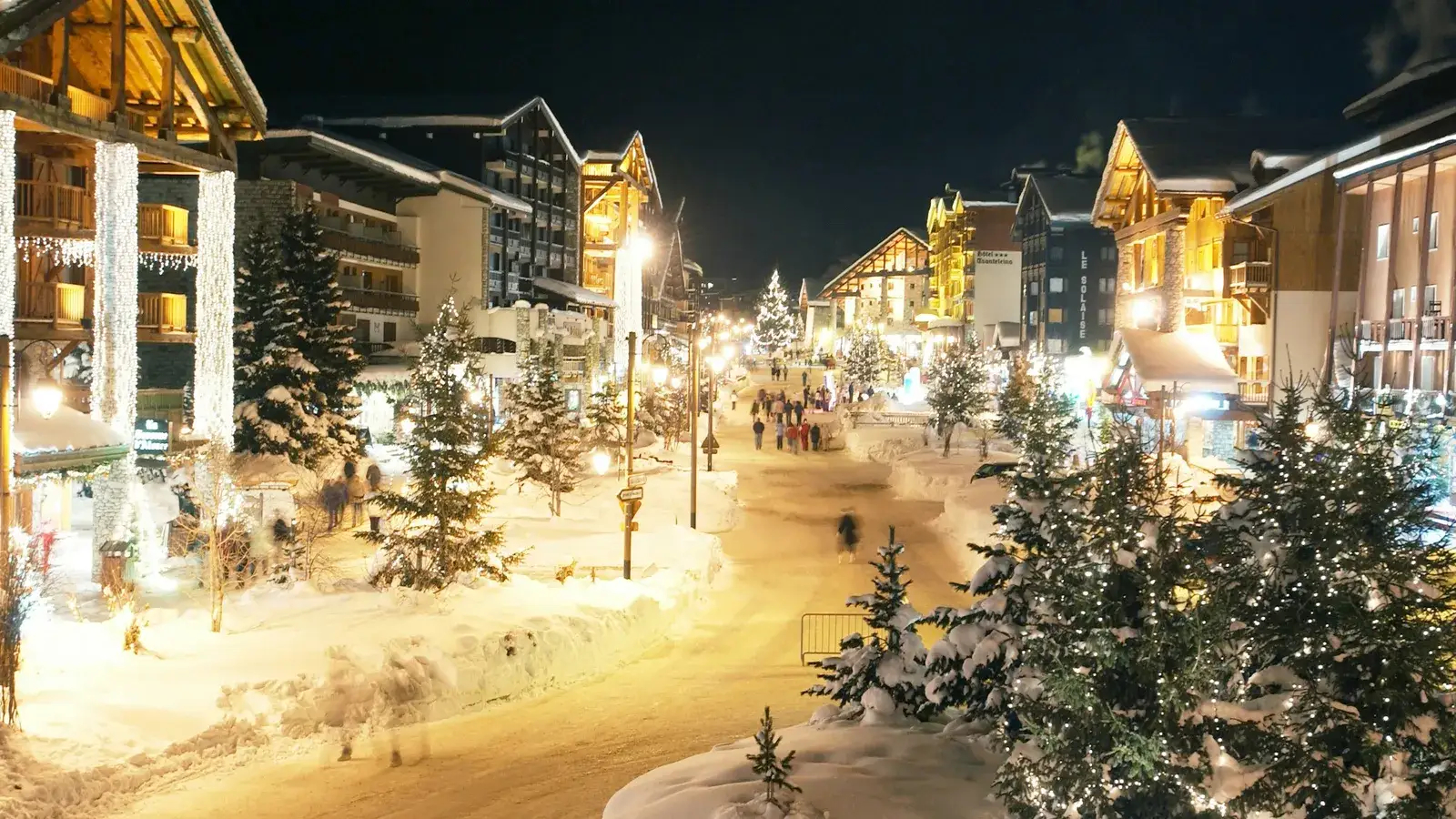 A snowy village street glowing with warm lights in the evening