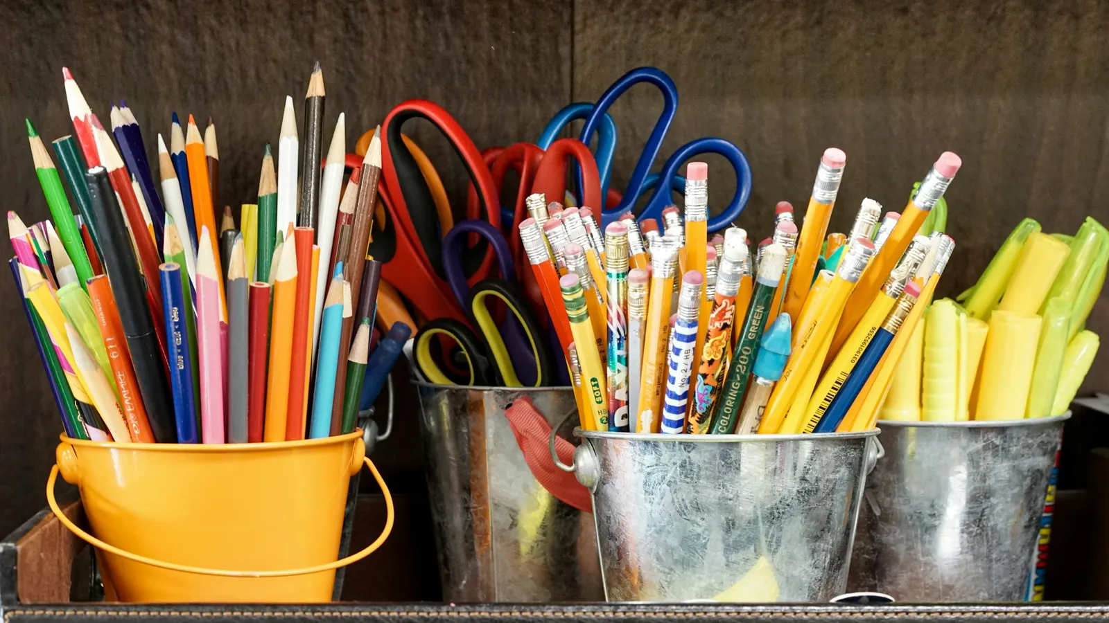 Pots full of coloured pencils, scissors and markers on a classroom shelf