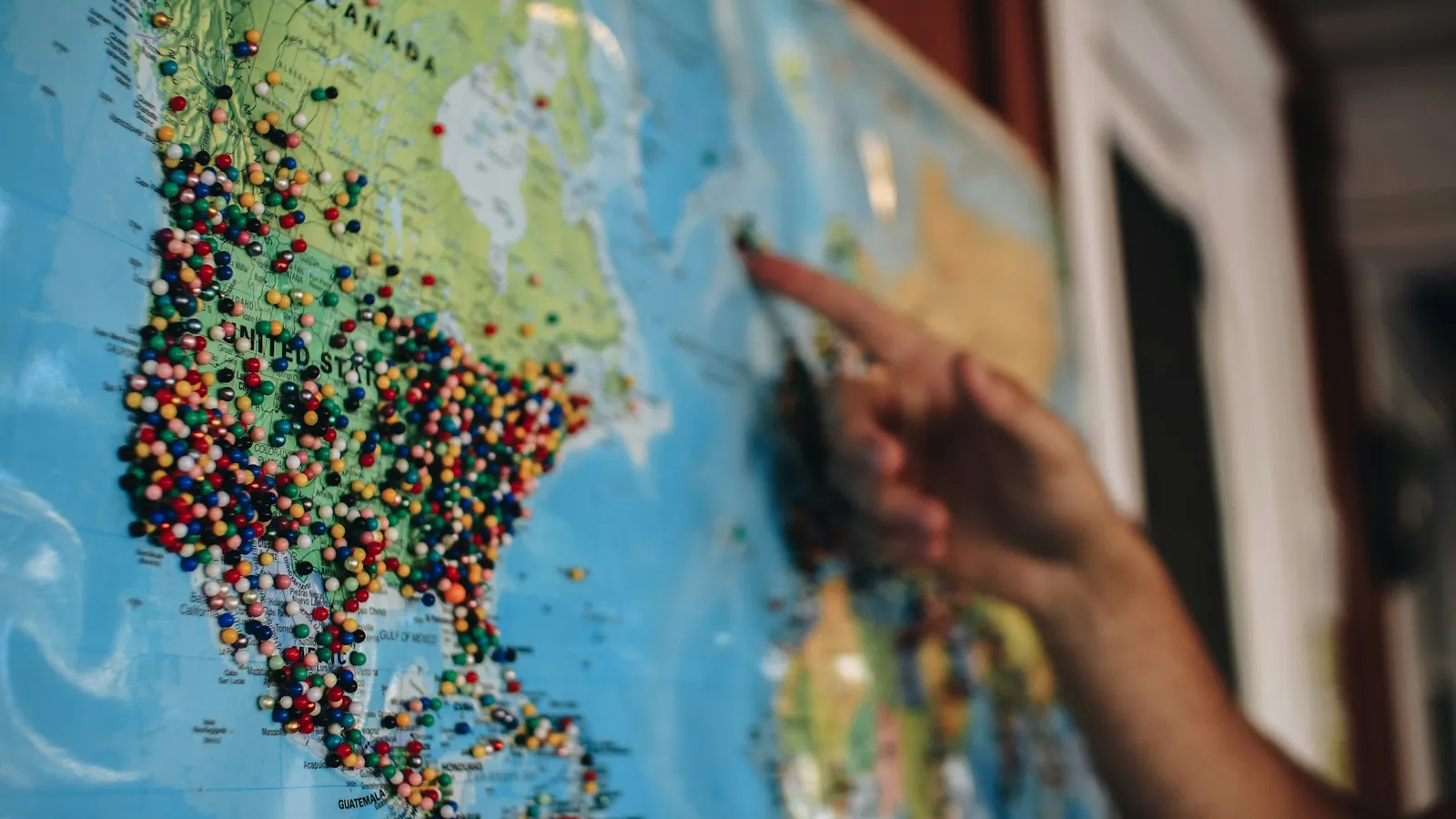 A hand pointing at a world map covered in coloured pins