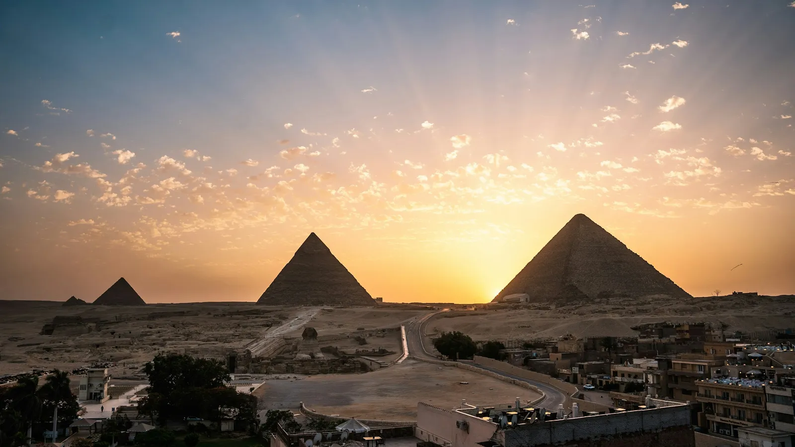 The pyramids of Giza at sunrise, with rays of light across the sky