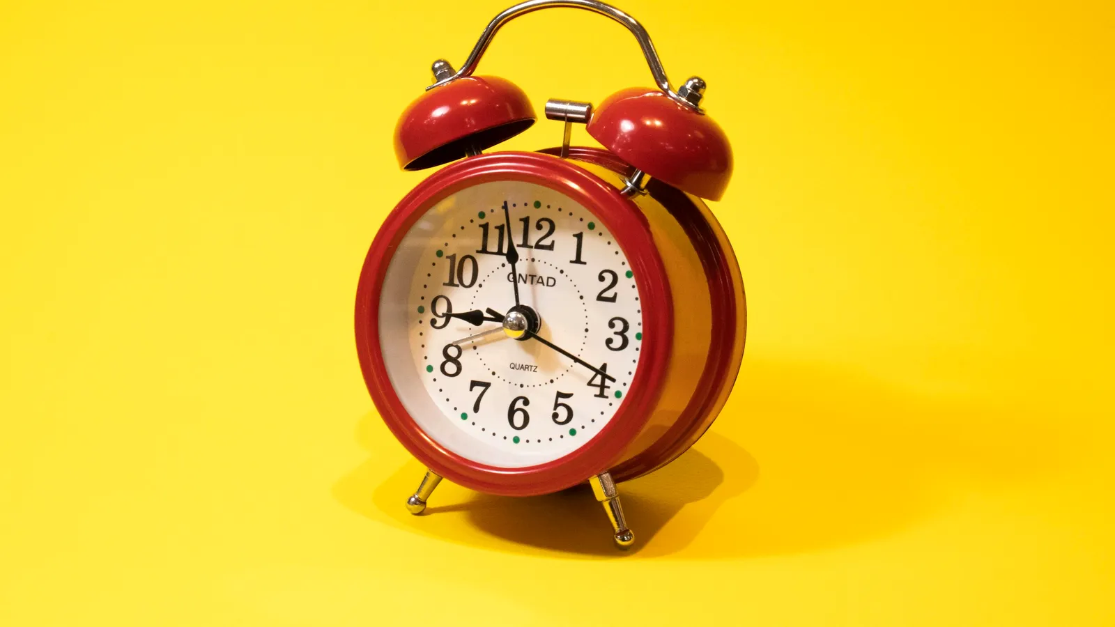 A red alarm clock against a bright yellow wall