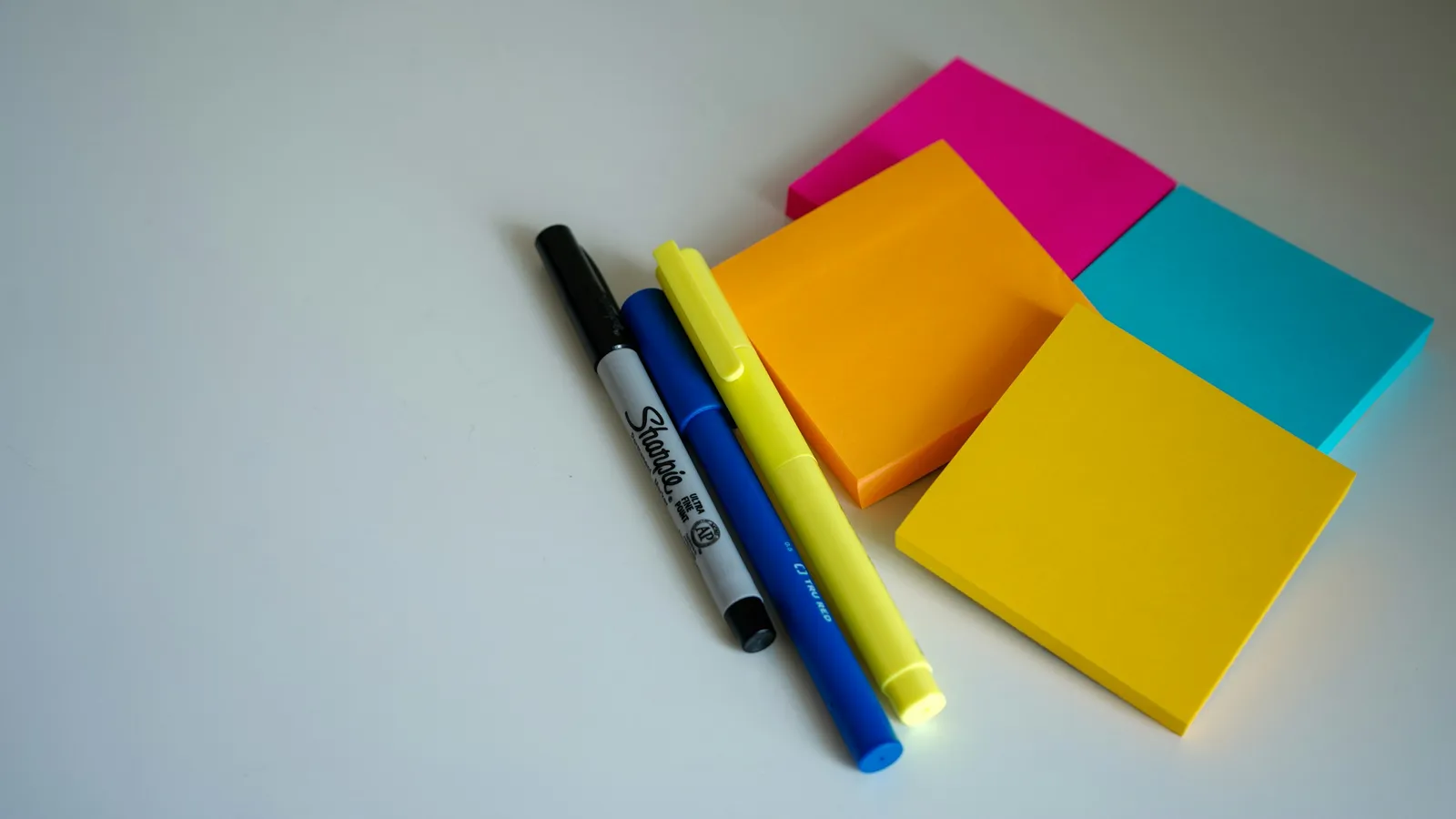 Bright sticky notes in pink, blue and yellow beside two highlighters