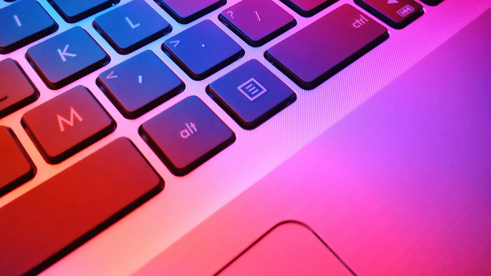 A laptop keyboard lit in pink and purple