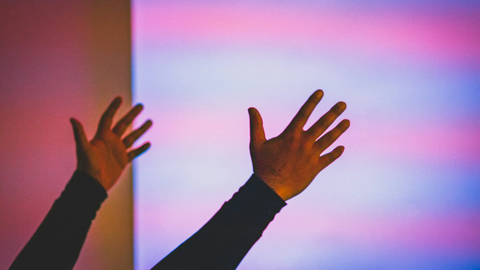 Raised hands against a wall of soft pink and blue light