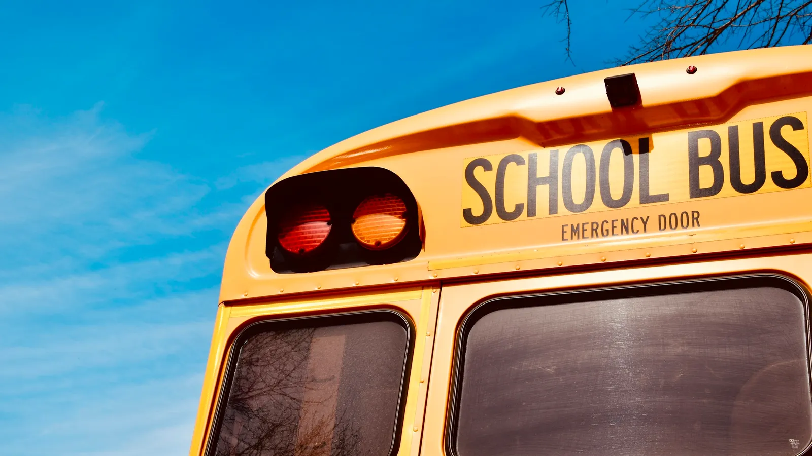 The back of a yellow school bus against a bright blue sky