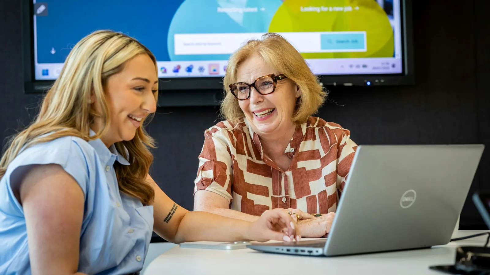 Two colleagues laughing together over a laptop