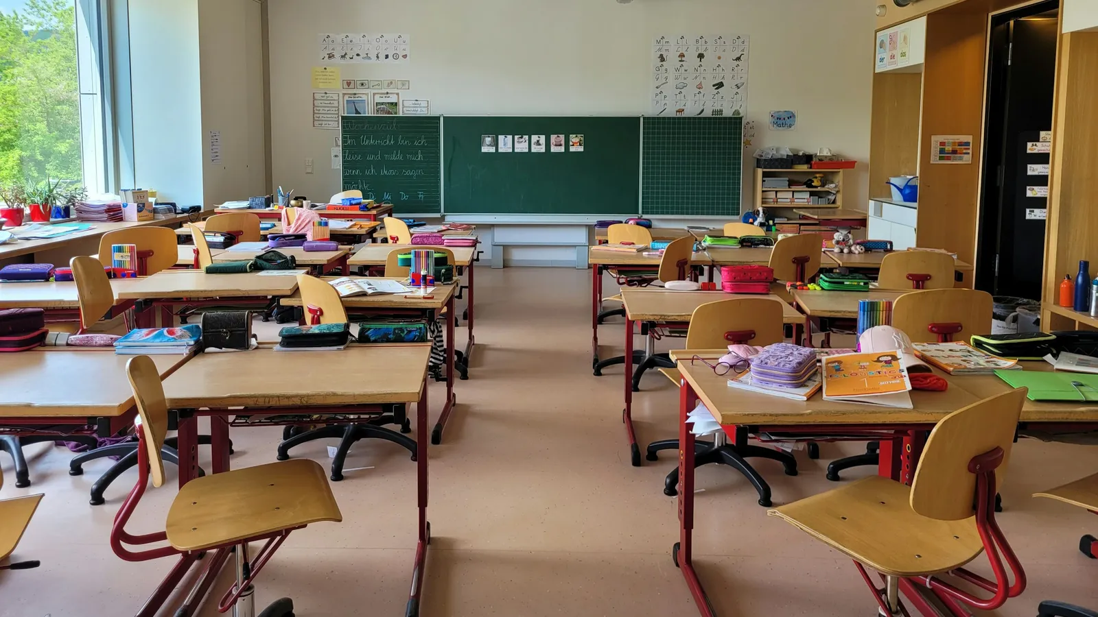 A bright, empty classroom with desks, chairs and a green board