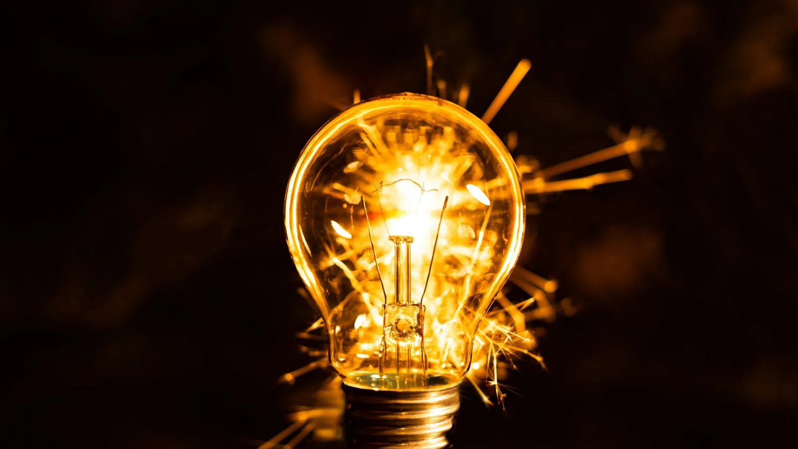 A light bulb bursting with golden sparks in the dark
