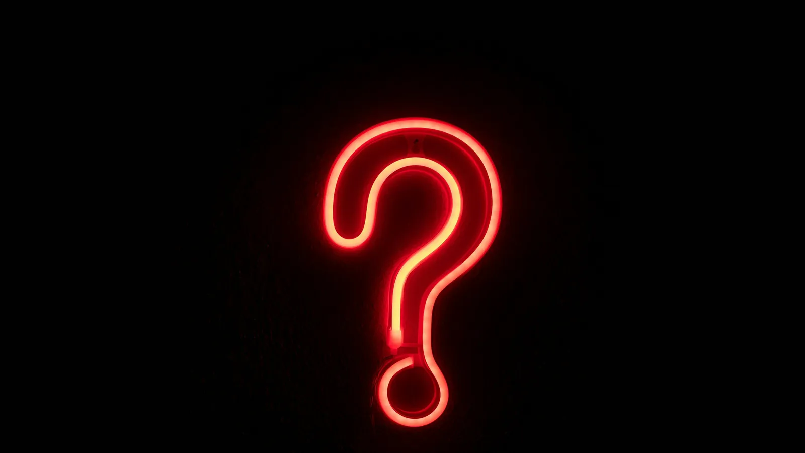 A glowing red neon question mark on a black wall