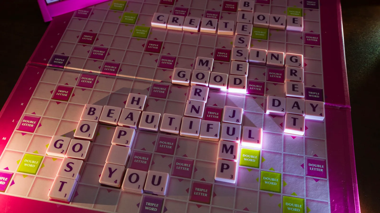 Letter tiles on a word game board, lit in neon pink