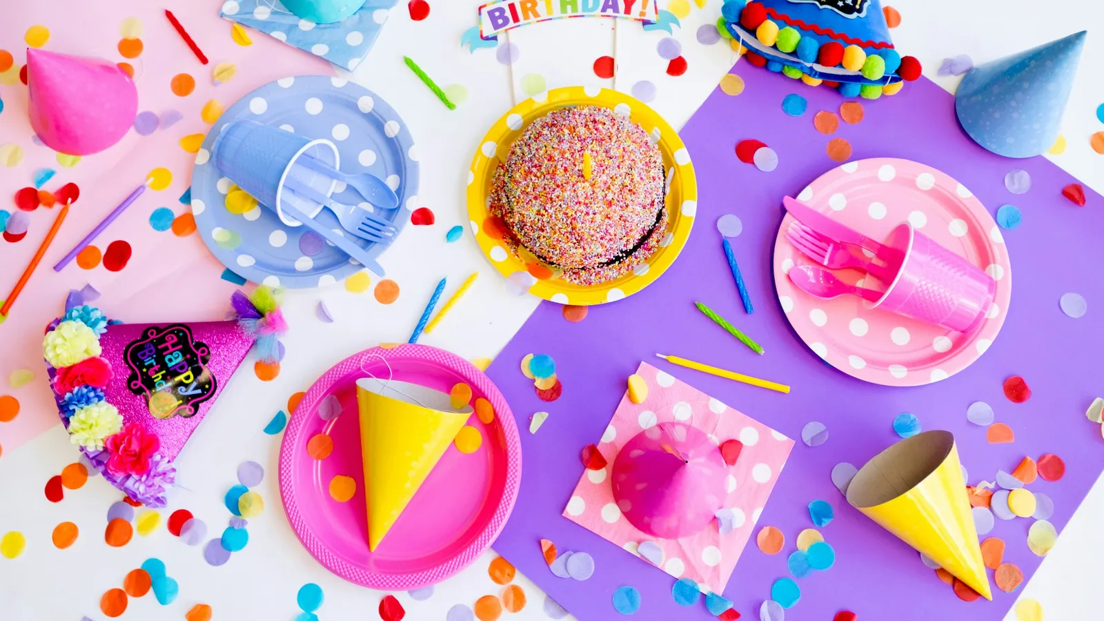 A birthday party table with a cake, party hats and colourful plates